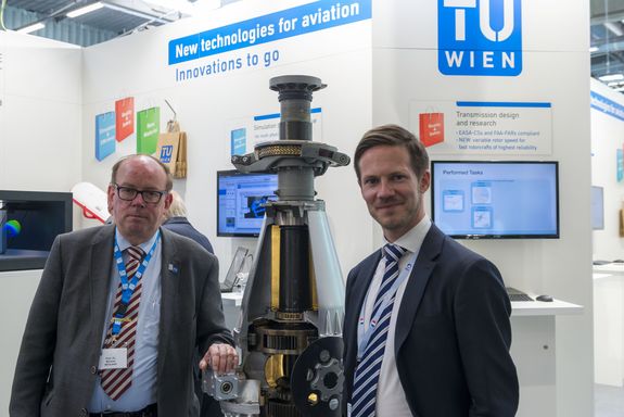 2 people at the TU Wien stand, between them a gearbox of a BO 105 helicopter