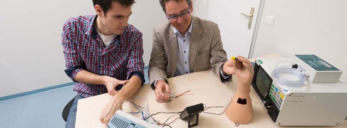 Zwei Männer in einem Raum Testen eine kleine Maschiene, die auf dem Tisch steht.