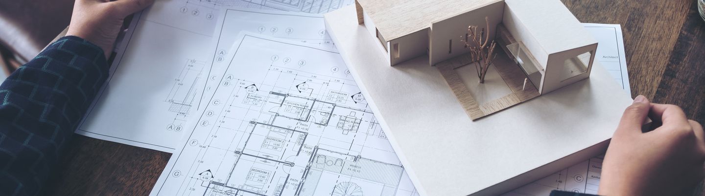 An architect working on an architecture model with shop drawing paper on table