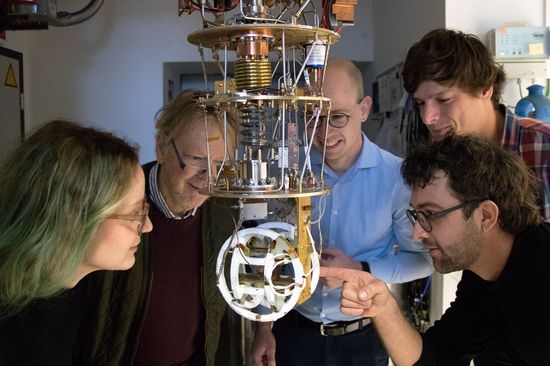 Fünf Personen rund um eine technische Anlage aus Röhren und Metallverstrebungen, die von der Decke hängt.