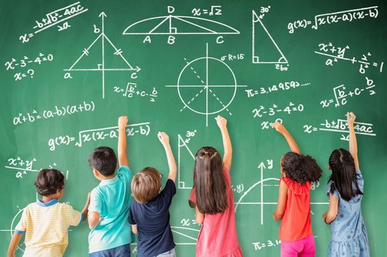 A group of pupils are standing at a blackboard doing maths.