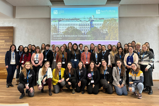 Group photo with about 40 women in front of a screen showing the main building of the TUW.