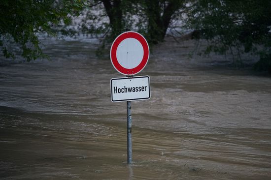 Verkehrsschild mit Aufschrift "Hochwasser" an einer überfluteten Straße