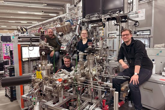 Vier Personen rund um ein kompliziertes Messgerät mit vielen metallischen Teilen und Kabeln