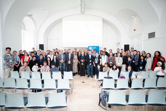 Group photo in a light-coloured room, vaulted ceiling. White rows of seats in the foreground.