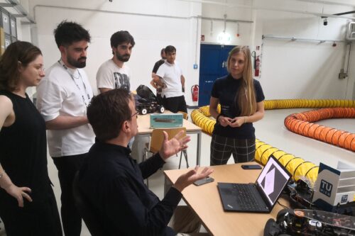 Professor and students discussing. Model racing car in the front.